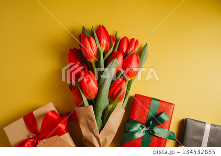 Mothers' day. Red tulips with gift boxes. Easter holiday. Yellow background. Flat lay, copy space 134532885