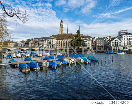 Panoramic view of historic Zurich cityscape with covered boats docked along Lake Zurich waterfront under cloudy sky 134534209