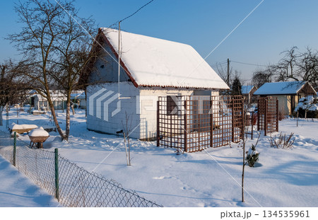 Snowy Winter Garden with Bench and Small Houses at Sunrise 134535961