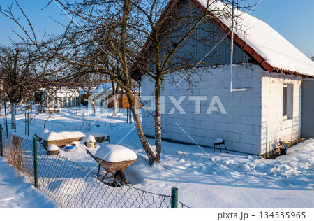 Snowy Winter Garden with Bench and Small Houses at Sunrise 134535965