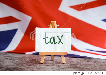 Paper note with words TAX on National symbol of Great Britain. British wave the UK silky flag background. Tax planning system and economy policy  134538431