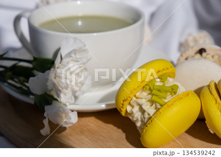 Green latte matcha with yellow and white sweet macaron on messy bed. Concept of holiday breakfast morning tea drink. Cozy minimalist superfood vibrant colors healthy eating. Organic caffeine-free Green latte matcha with yellow and white sweet macaron on messy bed. Concept of holiday breakfast morning tea drink. Cozy minimalist superfood vibrant colors healthy eating. Organic caffeine-free 134539242