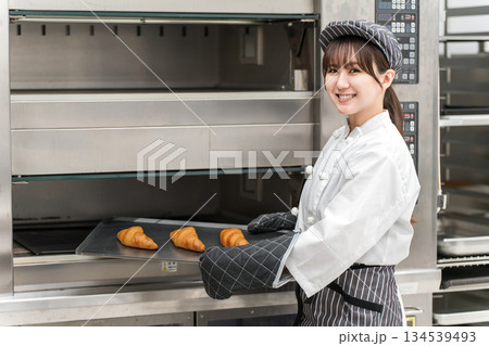 オーブンからパン,クロワッサンを取り出す調理スタッフの女性 134539493