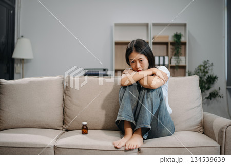 Asian woman suffering from flu symptoms, covered with a blanket on a sofa. Concept of illness, healthcare, and recovery. Asian woman suffering from flu symptoms, covered with a blanket on a sofa. Concept of illness, healthcare, and recovery. 134539639