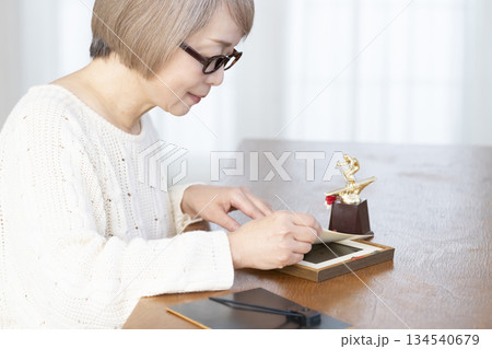 リビングで写真を額に入れて飾るシニア女性 リビングで写真を額に入れて飾るシニア女性 134540679
