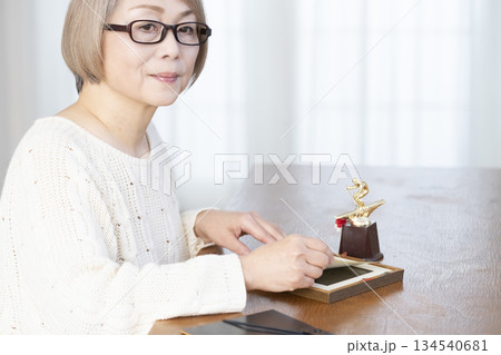リビングで写真を額に入れて飾るシニア女性 リビングで写真を額に入れて飾るシニア女性 134540681