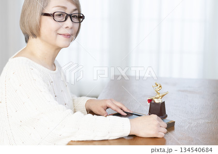 リビングで写真を額に入れて飾るシニア女性 リビングで写真を額に入れて飾るシニア女性 134540684