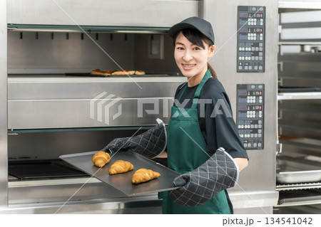 オーブンからパン,クロワッサンを取り出す調理スタッフの女性 134541042