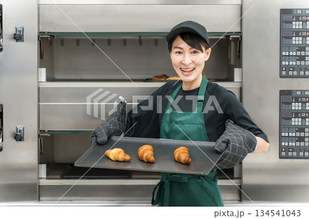 オーブンからパン,クロワッサンを取り出す調理スタッフの女性 134541043