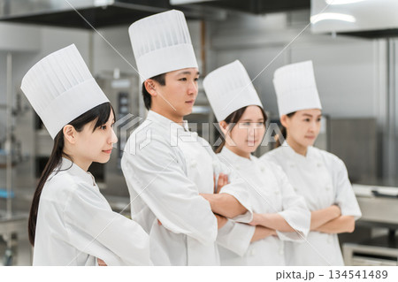 厨房・キッチンに立つコックコート姿の調理師・シェフ・コックの男女 134541489