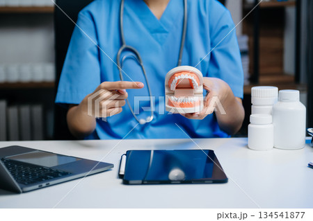 Dentist sitting at table with jaw samples tooth model and working with tablet and laptop in dental modern office 134541877