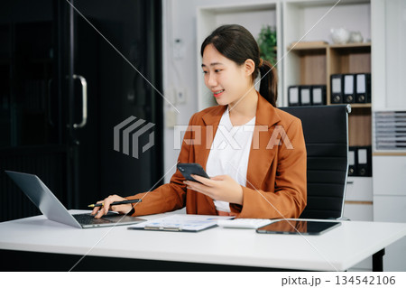 Asian woman using laptop and tablet while sitting at her working place. Asian woman using laptop and tablet while sitting at her working place. 134542106