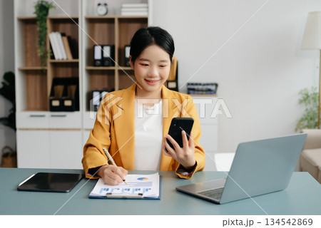 Confident Asian woman with a smile standing holding notepad and tablet at the office. Confident Asian woman with a smile standing holding notepad and tablet at the office. 134542869