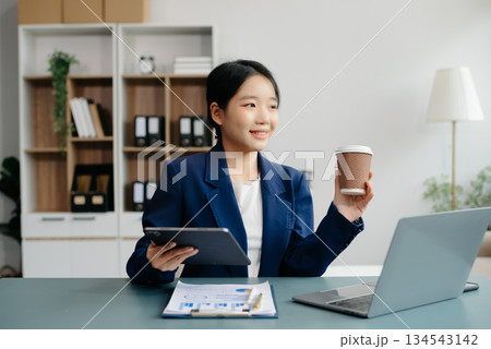 Confident Asian woman with a smile standing holding notepad and tablet at the office. 134543142