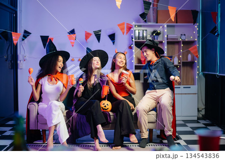 Halloween party with friends in costumes, enjoying drinks, food, and festive decorations. Perfect for autumn gatherings Halloween party with friends in costumes, enjoying drinks, food, and festive decorations. Perfect for autumn gatherings 134543836