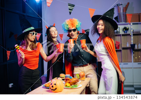 Halloween party with friends in costumes, enjoying drinks, food, and festive decorations. Perfect for autumn gatherings Halloween party with friends in costumes, enjoying drinks, food, and festive decorations. Perfect for autumn gatherings 134543874