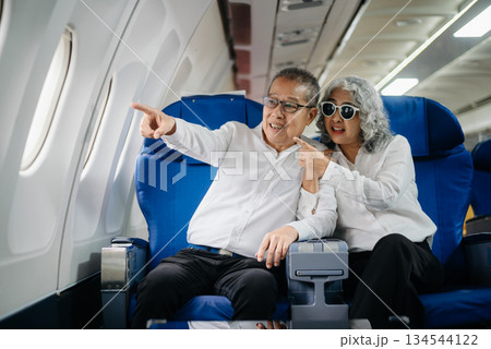 Senior Asian couple capturing memories on a plane, blending travel with technology. Smiling, stylish, Senior Asian couple capturing memories on a plane, blending travel with technology. Smiling, stylish, 134544122