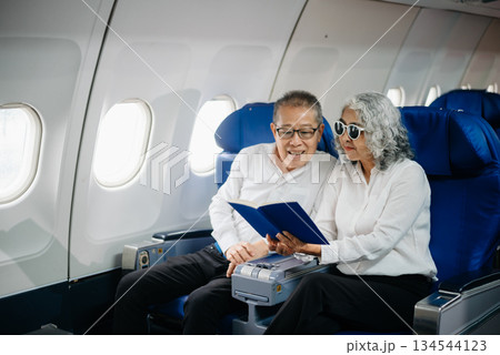 Senior Asian couple capturing memories on a plane, blending travel with technology. Smiling, stylish, 134544123