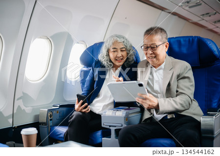 Senior Asian couple capturing memories on a plane, blending travel with technology. Smiling, stylish, 134544162