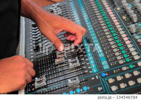 Closeup shot of sound engineer adjusting faders on a black audio mixing board during a live event or recording session. Closeup shot of sound engineer adjusting faders on a black audio mixing board during a live event or recording session. 134546784