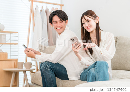 家のリビングでソファーに座りスマホを見ながら会話する若いアジア人夫婦 家のリビングでソファーに座りスマホを見ながら会話する若いアジア人夫婦 134547402