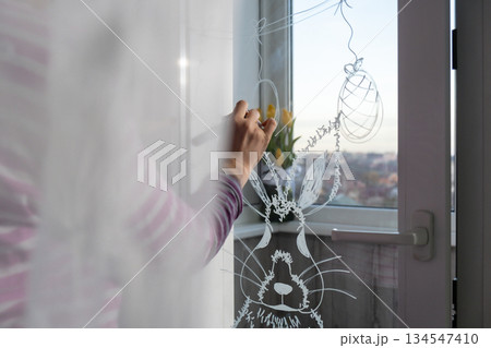 Zero cost responsible holiday decor economically driven. Female hand painting Easter bunny rabbit on window glass indoor at home. Affordable alternative Easter springtime seasonal tradition ideas Zero cost responsible holiday decor economically driven. Female hand painting Easter bunny rabbit on window glass indoor at home. Affordable alternative Easter springtime seasonal tradition ideas 134547410