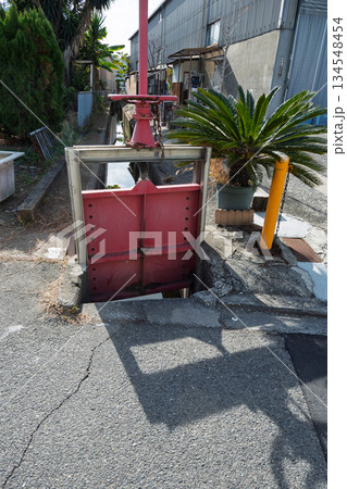 住宅街の水路で稼働する赤いハンドルの水門:適切にメンテナンスされた農業水利インフラ 正面から 住宅街の水路で稼働する赤いハンドルの水門:適切にメンテナンスされた農業水利インフラ 正面から 134548454