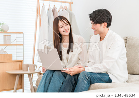 家のリビングでソファーに座りパソコンを見る若いアジア人夫婦,カップル 134549634