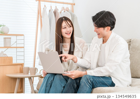 家のリビングでソファーに座りパソコンを見る若いアジア人夫婦,カップル 家のリビングでソファーに座りパソコンを見る若いアジア人夫婦,カップル 134549635