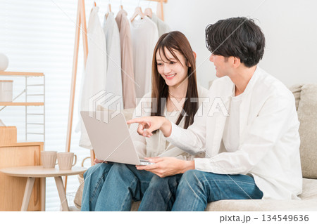 家のリビングでソファーに座りパソコンを見る若いアジア人夫婦,カップル 134549636