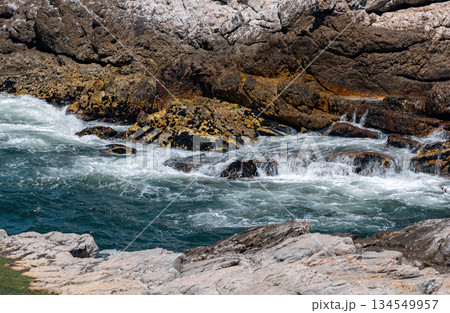 Waves crashing against rocky shore under clear blue sky, ocean coastal landscape 134549957