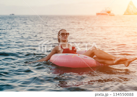 Woman, floating, sea. Relaxing woman floating on inflatable donut ring in calm sea at sunset with copy space. Woman, floating, sea. Relaxing woman floating on inflatable donut ring in calm sea at sunset with copy space. 134550088