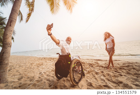 Disabled man in a wheelchair with his wife on the beach. Disabled man in a wheelchair with his wife on the beach. 134551579