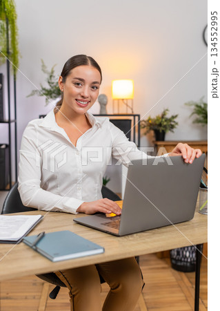 Young businesswoman opens laptop smiles starts typing and begins fresh workday with focus and energy Young businesswoman opens laptop smiles starts typing and begins fresh workday with focus and energy 134552995
