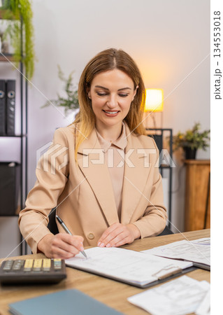 Businesswoman sorts receipts uses calculator balances budget signs final contract with pleased smile Businesswoman sorts receipts uses calculator balances budget signs final contract with pleased smile 134553018