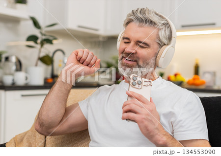 Middle-aged man turns on playlist in headphones nods to beat smiles relax takes break from work calm 134553090