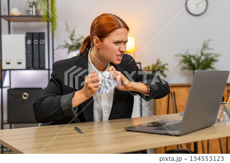 Young businesswoman finds debit credit mismatch on laptop crumples paper throws it aside in panic Young businesswoman finds debit credit mismatch on laptop crumples paper throws it aside in panic 134553123