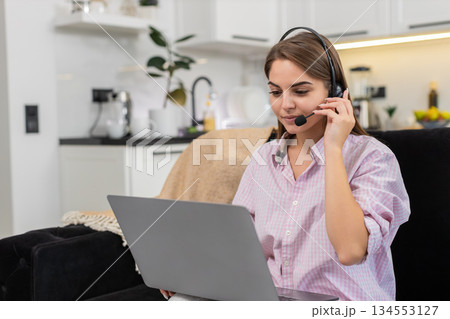 Young woman with headset starts laptop video call with client greets listens asks helpful questions Young woman with headset starts laptop video call with client greets listens asks helpful questions 134553127