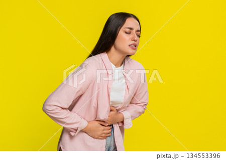 Young woman bending forward rubbing stomach showing painful expression suffering from abdominal ache 134553396