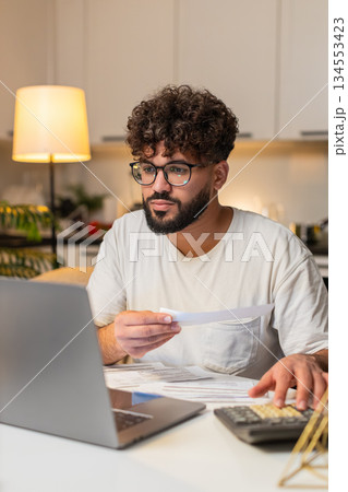 Arabian man balances accounts with laptop and calculator enters sums marks paid checks late night up Arabian man balances accounts with laptop and calculator enters sums marks paid checks late night up 134553423