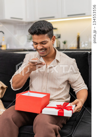Indian man opens gift box surprised takes smartphone photo thanks friends for present with big smile Indian man opens gift box surprised takes smartphone photo thanks friends for present with big smile 134553556
