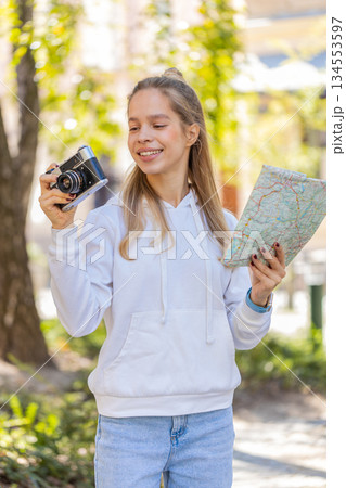 Caucasian young woman tourist looking at city map, making photo pictures on retro vintage camera 134553597
