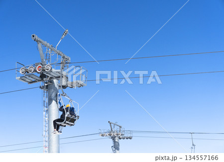 Ski chair lift over blue sky. Ski lift empty ropeway on hilghland mountain winter. Ski chairlift cable way with people enjoy skiing and snowboarding 134557166