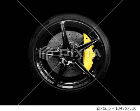 Car alloy wheel and tyre isolated on black background. New alloy wheel with tire and yellow carbon ceramic brakes. Alloy rim isolated. Car wheel disc. Car spare parts. 134557310