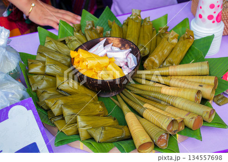 High angle close-up shot of various Indonesian traditional sweet market snacks, including Clorot and Lepat, arranged on banana leaves with a coconut bowl. 134557698