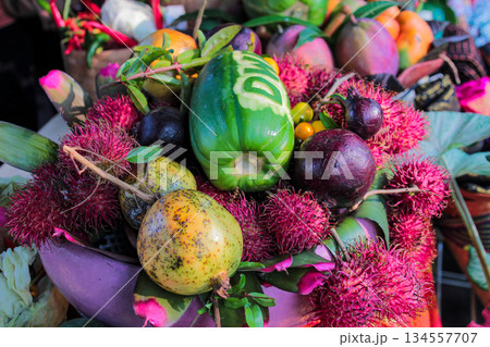 Abundant and colorful composition of exotic Southeast Asian fruits featuring bright pink rambutans, a carved green papaya, and dark purple fruits, captured outdoors. Abundant and colorful composition of exotic Southeast Asian fruits featuring bright pink rambutans, a carved green papaya, and dark purple fruits, captured outdoors. 134557707