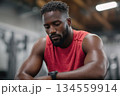 Man resting between sets at the gym while checking his smartwatch 134559914