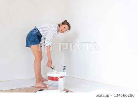 Portrait young adult beautiful single happy woman painting wall paint roller brush white color living room moving new home flat . Female painter decorating interior renovation residential apartment Portrait young adult beautiful single happy woman painting wall paint roller brush white color living room moving new home flat . Female painter decorating interior renovation residential apartment 134560286