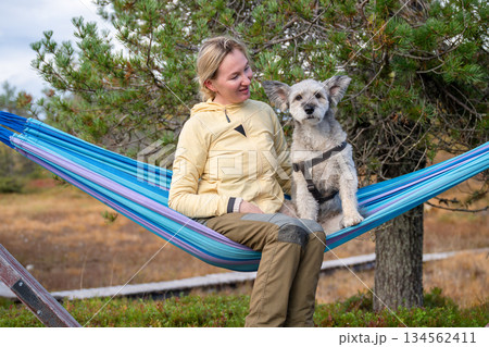 Woman relaxing in hammock with dog wearing outdoor clothing in forest nature Woman relaxing in hammock with dog wearing outdoor clothing in forest nature 134562411