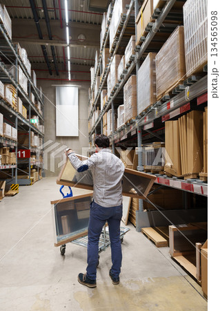 Man loading furniture panels onto shopping cart in warehouse aisle, home improvement, DIY shopping Man loading furniture panels onto shopping cart in warehouse aisle, home improvement, DIY shopping 134565098